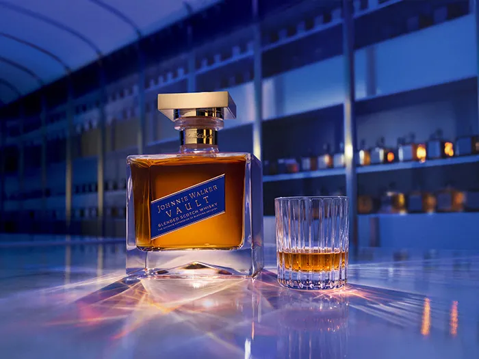 Johnnie Walker Vault Blended Scotch Whisky: Flasche mit goldenem Verschluss neben einem gefüllten Tumbler